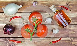 Top down view on raw uncooked isolated white and red onions, tomatoes vine, bottle olive oil and chillies. Brown natural rustic