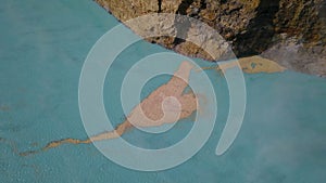 Top down view of sediments floating just below the surface of a turquoise volcanic lake. The camera moves upwards over photo