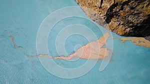 Top down view of sediments floating just below the surface of a turquoise volcanic lake. The camera moves upwards over photo