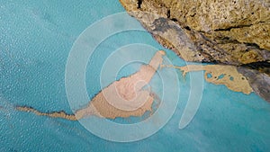 Top down view of sediments floating just below the surface of a turquoise volcanic lake. The camera moves upwards over photo