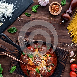 Top down view of a skillet filled with saucy meatballs surrounded by pasta ingredients and copy space in the middle.