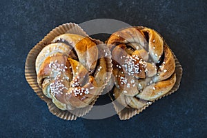 Top down view of two fresh cinnamon buns with sugar on top placed on rustic dark stone table