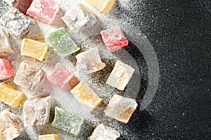 Top down view of a variety of turkish delight candies in different colors and taste, scattered on a black kitchen board, covered