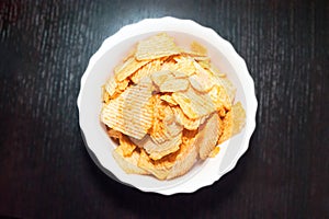 Top-Down View of a White Bowl of Ridged Potato Chips on Dark Wooden Background