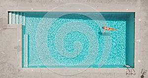 Top down view of a woman in redre swimsuit lying on her back in the pool.