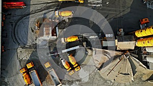 Top down view of yellow trucks some parked and one driving on an industrial site
