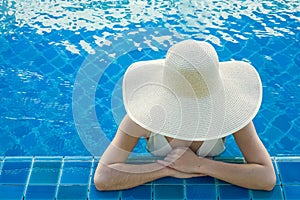 Top- down of young woman , wearing white straw hat and white bikini relaxing in warm summer swimming pool with blue water on a sun