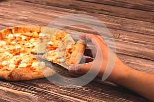 Top edge view on man`s hand taking one slice of big delisious four-cheese pizza on wooden background or table with copyspace for