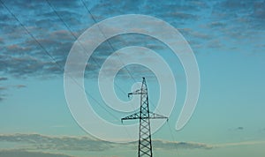 Top of electricity pylon and power lines in front of calm blue evening sky and clouds