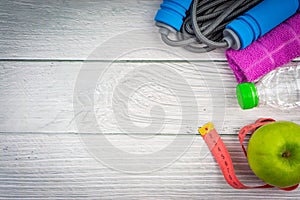Top or flat lay view of towel, water, apple fruit, sport shoes and skipping rope with copy space area on wooden background