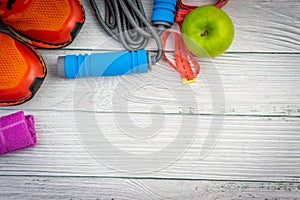 Top or flat lay view of towel, water, apple fruit, sport shoes and skipping rope with copy space area on wooden background