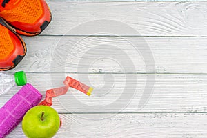 Top or flat lay view of towel, water, apple fruit, sport shoes and skipping rope with copy space area on wooden background