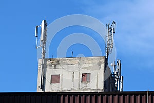 Top floor of old concrete industrial building with two windows closed with metal blinds and multiple cell phone antennas