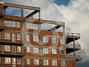 Top floors of a newly built red brick housing block with plastic windows covered with foil and gray concrete balconies