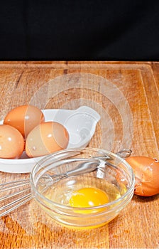 Glass bowel of egg with whisk, egg shell and three brown eggs