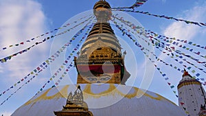 Top of golden colored Buddhist stupa in temple complex Swayambhunath, Kathmandu, Nepal decorated with prayer flags flying.