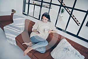 Top high above angle photo of concentrated girl sit on brown leather divan use phone read feednews post comments hold