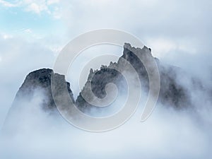 Top mountains in white clouds. The edge of the sheer cliff is barely visible due to low clouds and dense fog. White cloud