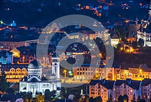 Top panoramic view of illuminated orthodox church and old buildings in downtown of Sighisoara, Romania at night