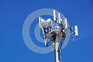 Top part of cell phone communication tower with multiple antennas against a blue sky