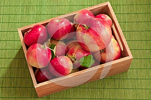 Top perspective view of wet apples with water drops in a small bamboo crate on green background