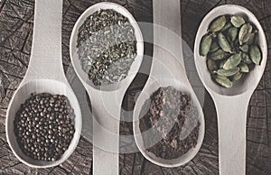 top photo of various spices in spoons on a wooden texture: coriander seeds, oregano dried, milled cinnamon, fennel