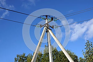 Top of a power line pole with wires and insulators against a blue sky with clouds