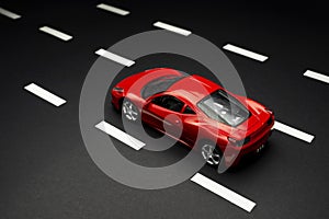 Top and rear view of Red toy sports car on an asphalt road with road lanes