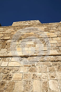 Top section of antique castle wall of old high sandy limestone under clear cloudless blue sky on sunny day