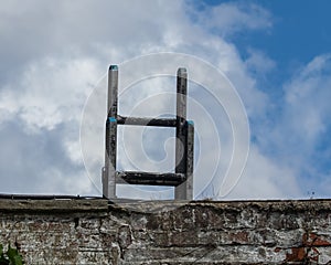 Top section of long metal ladder leaning on aged brick wall against cloudy blue sky