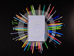 Top shot of a blank ruled notebook with scattered pencils and crayon colors on black background