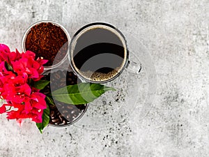 Top shot of coffee powder, black americano, roasted beans covered with flowers or leaves with copy space