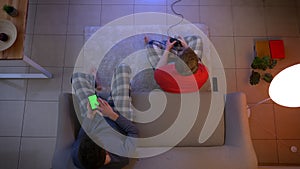 Top shot of friends in sleepwear playing videogame with joystick and working with smartphone in the living room.