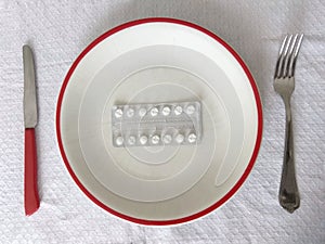 Top shot of a white plate edged with red a tablet leaf on knife and fork around on