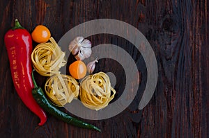 Top viev Italian raw nest pasta with vegetables tomatoes, chili peppers, garlic, spices on a dark wooden background