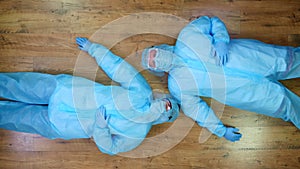 Top view. 2 Exhausted, tired medical workers, doctors or nurses, in special protective uniforms, masks, goggles