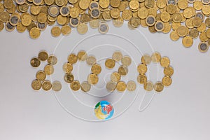 Top view of 2020 written with coins, in between a heap of coins and a earth model, on gray background