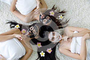 Top view for 3 asian women sleep on white carpet, she has long black hair, all smile look happy and face still masked with black