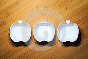 Top view of 3 white ceramic bowls of apple shape design on wood dining table background