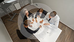 Top view of 4 business people sitting at a table and discussing blueprints. Designers engineers at a meeting.