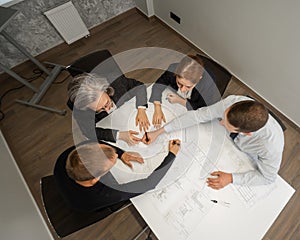 Top view of 4 business people sitting at a table and discussing blueprints. Designers engineers at a meeting.