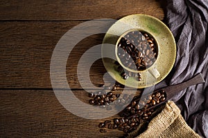 Top view above of Black coffee beans in brown ceramic cup with coffee beans roasted in burlap sack bag on wooden table background