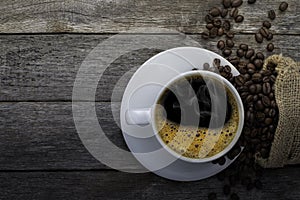 Top view above of Black hot coffee with smoke and milk foam in white ceramic cup with coffee beans roasted in sack bag on dark sto