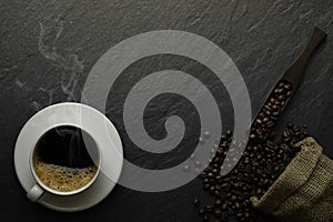 Top view above of Black hot fresh coffee with smoke and milk foam in a white ceramic cup with coffee beans roasted in burlap sack