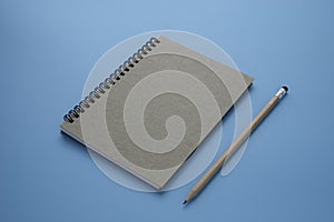 Top view above of brown spiral notebook and pencil isolated on blue background for design a mockup.