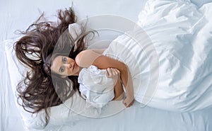 Top view from above to an attractive, young, sexy, wild, windblown, brunette, portrait of woman in bed hugging the bedspread, copy
