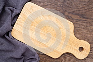 Top view above of Wooden chopping board with napkin on dark table background.