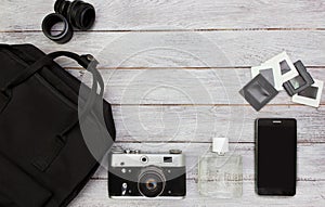 Top view accessories   -backpack, vintage camera,mobile phone,retro slides ,lens and parfume on white wooden background.Black and
