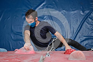 Top view of an active sporty man wearing protective face mask practicing rock climbing on artificial rock in a climbing wall