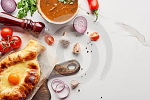 Top view of adjarian khachapuri, soup kharcho, vegetables and spices on marble texture.